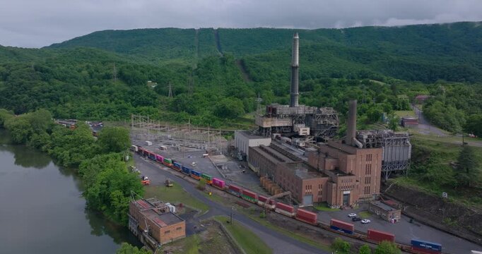Former coal power plant complex beside river with passing freight train, drone orbit establishing