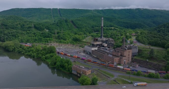 Glen Lyn industrial power station surrounded by Appalachian forested hills, drone panoramic pullback establishing along highway
