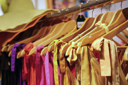 Row of colorful summer dresses on wooden hangers in a fashion boutique clothing store. Retail shopping and wardrobe concept.