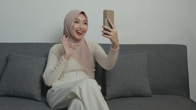 Attractive Asian Muslim woman wearing hijab is smiling while having a call with family or friends, isolated by white background.
