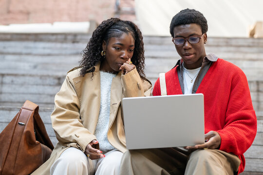 Thoughtful african american couple man and woman students sit outdoors with laptop after class, smart black male and female friends brainstorming and discussing studies, preparing for tests together.