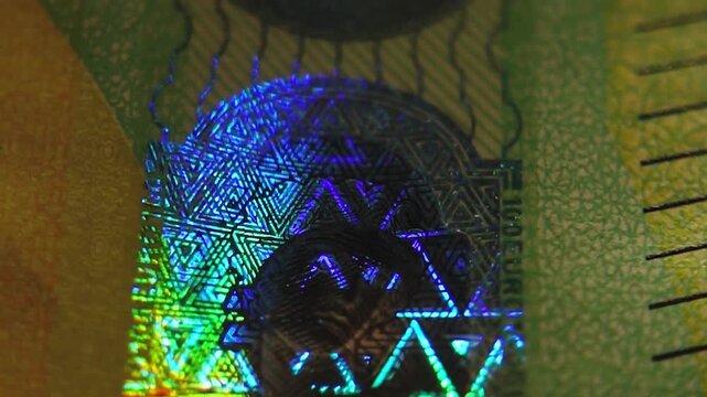 A close-up of the security holographic emblem on the 100 euro banknote. The hologram on the one hundred euro banknote glows in different colors. 4K slow motion video at 60 fps.
