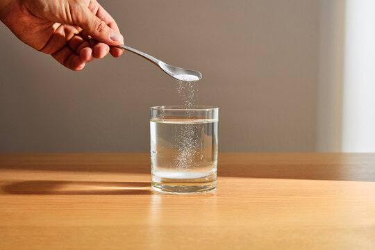 Hand pouring white powder from spoon into a glass of water
