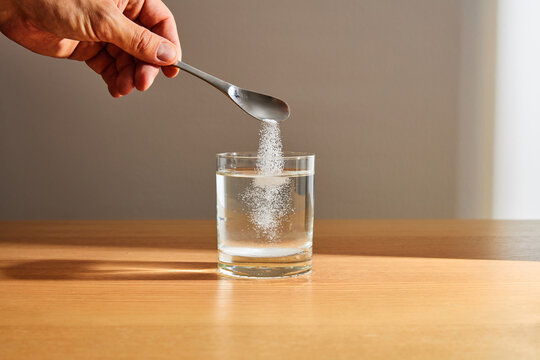 Hand Pouring White Powder from Spoon into Glass of Water