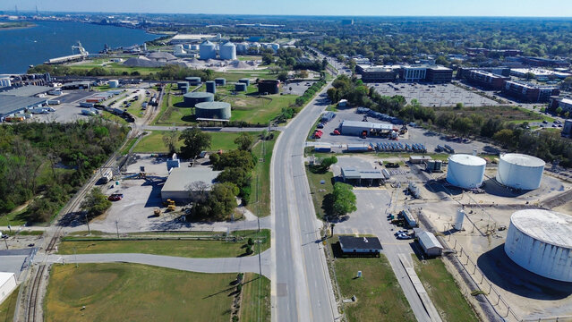 Rail tracks parallel highway transit paths near industrial warehouses. Logistics operations anchor busy landscape, connecting regional freight hubs across coastal basin in North Charleston, SC