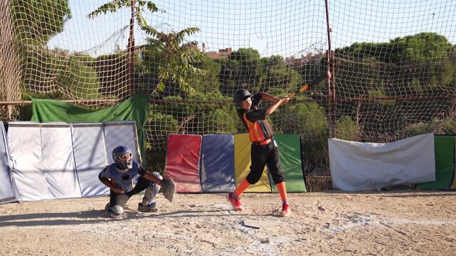 Teenage batter swinging the bat, hitting the ball, and starting his run to first base. Young catcher waiting behind the home plate