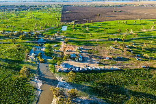 Aerial scene showcasing the Pilliga Artesian Bore Baths and adjacent campground, with a winding creek flowing through the lush green bushland and cultivated farmland stretching across the background