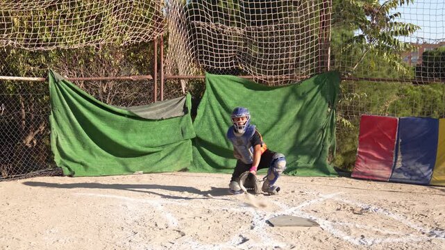 Slow motion of a youth league baseball catcher in full gear blocking a wild pitch in the dirt during practice at the home plate