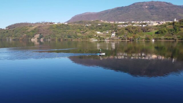 Aerial 4K drone video of a person canoeing on the calm, reflective waters of Lake Caldonazzo in Trentino, Italy, surrounded by beautiful Alpine mountains.