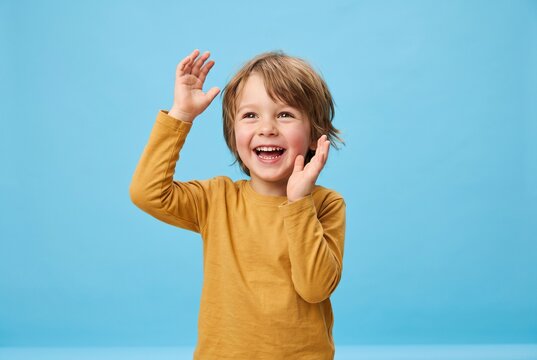 Joyful young child beaming with hands playfully raised on a serene blue canvas