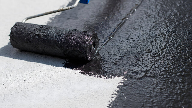 Applying black waterproof sealant coating on concrete floor with a paint roller