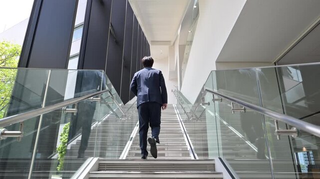  [Slow Motion] Video of a mid-level business executive walking up the stairs in an office&mdash;full-body shot of his back, without face
