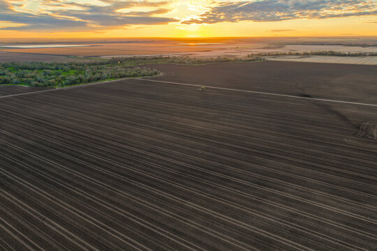 Aerial view capturing sunrise over cultivated farmland near Pilliga, with warm golden light highlighting the natural patterns and textures in the soil to create a striking rural landscape.