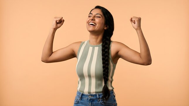 Cheerful young woman with long dark braided hair celebrating a major personal victory while wearing a striped ribbed tank top against a soft orange background