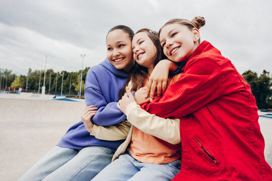Three smiling teenage girls hugging and sitting together outdoors