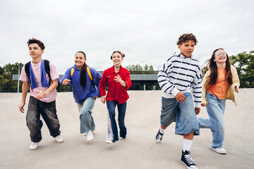 Obraz premium Group of happy multicultural teenagers running together at skate park outdoors