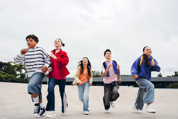 Obraz premium Portrait of happy group of teenagers running together in urban skate park