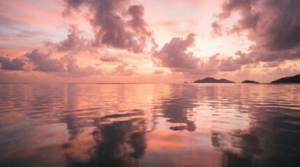 Obraz premium Sunset glow illuminates a calm ocean surface where soft pink clouds drift lazily above the distant horizon line reflecting vibrant colors across the gentle ripples of the peaceful tropical water.