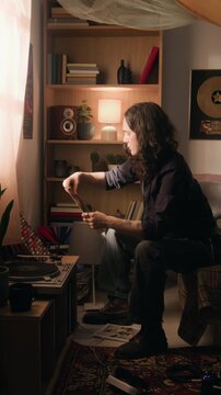 Vertical video of young man selecting vinyl record and playing it on turntable. Footage for music streaming apps, retro lifestyle promos, or hobbyist campaigns