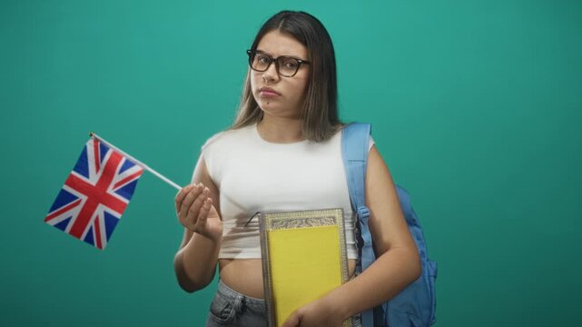 Young woman holding uk flag and books, hand extended toward flag while wearing backpack in studio; uncertainty study abroad.