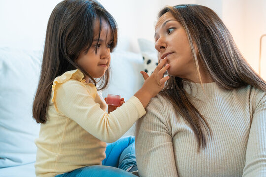 Little girl spreading cream to the face of her mother