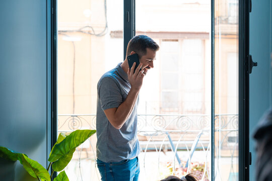 Man talking to the phone at home next to the balcony