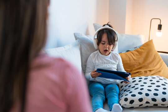 Cute girl using tablet and headphones sitting on the sofa