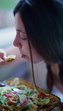 A young woman takes a bite of a healthy appetizer from a golden tray. She savors the flavorful, fresh snack.