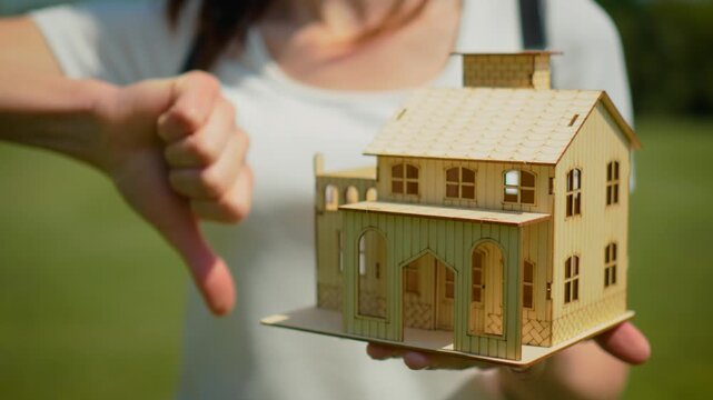 Real estate rejection concept with miniature home and thumbs down sign. Mortgage denial and failed property purchase scenario with housing loan refusal symbolism. Residential investment risk and