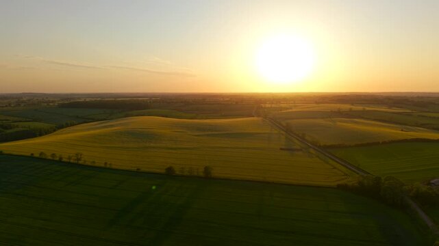 Aerial sunset landscape over patchwork farmland and green crop fields. Warm evening sunlight illuminating rolling countryside across spring season. Rural agricultural panorama featuring long shadows
