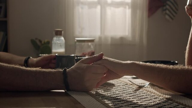 Close up of Caucasian young adult couple holding hands across dining table during breakfast. Footage represents relationship support, marriage counseling, or family insurance marketing concepts