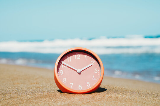a close-up of a salmon pink clock on the sand