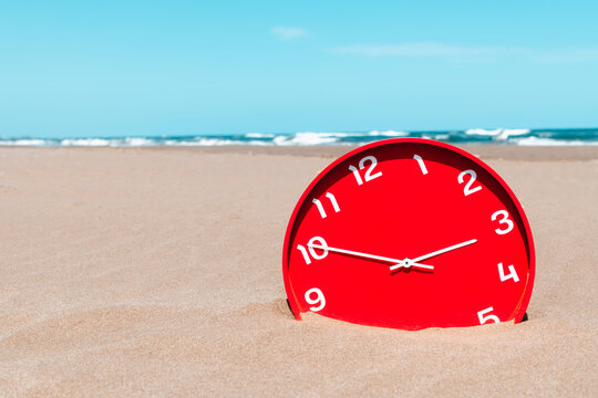 a red clock sinks into the sand on an empty beach