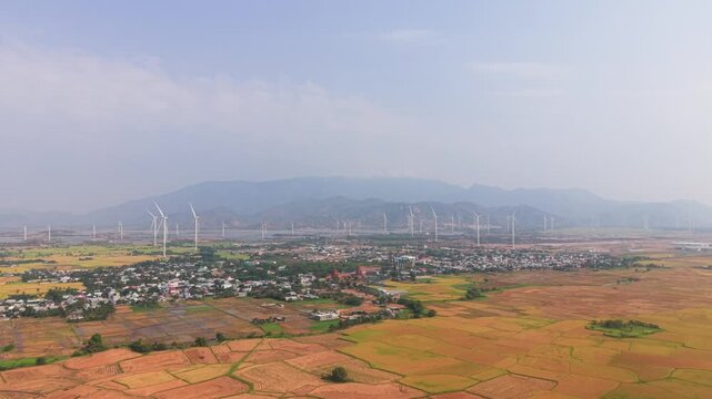 Dam Nai Wind Farm in Ninh Thuan Vietnam. Viewers can see wind turbines spinning and the surrounding landscape during daytime. Bright colors fill the area.