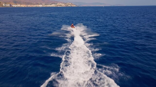 Drone footage rising and tilting up behind a jetski &mdash; riders surge across the Mediterranean as Almu&ntilde;ecar's resort skyline and mountain backdrop gradually fill the frame.