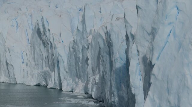 erito Moreno Glacier reveals towering blue ice walls, deep crevasses and fractured seracs above Lago Argentino in Los Glaciares National Park, Santa Cruz, Argentina, drone lateral slide shot.