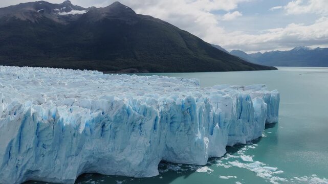 Perito Moreno Glacier rises above Lago Argentino in Los Glaciares National Park, Santa Cruz, Argentina, showcasing towering blue ice cliffs, crevasses and the Andes, slow drone oblique forward flight