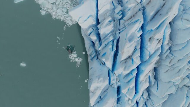 Perito Moreno Glacier reveals towering blue ice cliffs, deep crevasses and fractured seracs above Lago Argentino in Los Glaciares National Park, Santa Cruz, Argentina, top down drone ascent shot.