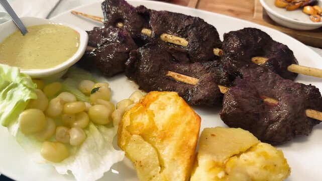 Close-up of traditional Peruvian dish Anticuchos served on a plate in a restaurant. Grilled marinated beef heart skewers with boiled potatoes and spicy sauces, authentic Peruvian cuisine. High quality