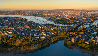 Aerial view of the Panmure basin and Tamaki Estuary and surrounding suburbs in Auckland, New Zealand, at sunset. Numerous sailboats are anchored in the calm waters. © Zenstratus