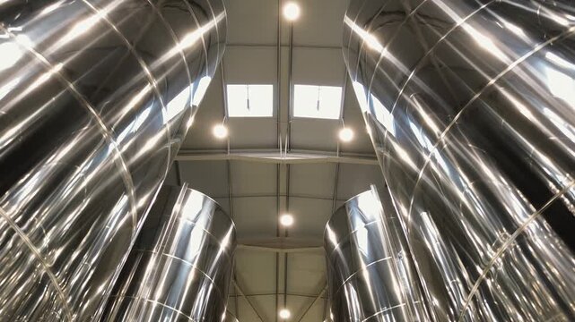 Bottom view looking up at huge shiny stainless steel storage silos or fermentation vats inside a modern processing facility