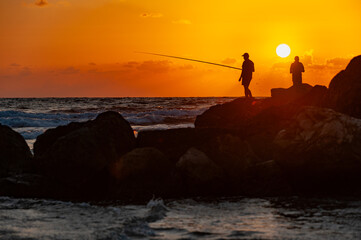 Fototapeta premium two silhouettes of fishers with ruffles against the backdrop of sunset