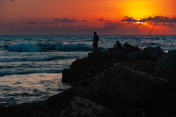 Fototapeta premium silhouette of two fishermans standing on a rock