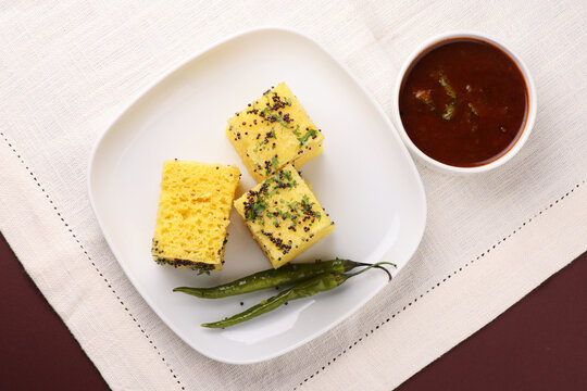 Khaman Dhokla made up of rice chana dal is a popular breakfast or Snacks recipe from Gujarat, India, served with Green chutney and fried chilli.. Selective focus

