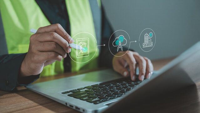 Smart construction planning concept worker using stylus on laptop with digital hologram of cloud computing integration smart building and IoT connectivity for remote industrial management