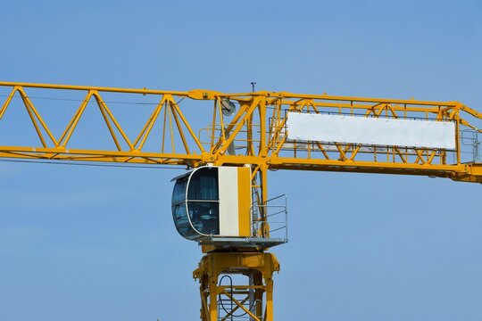 The operator cabin and jib of a bright yellow tower crane stand out against a clear blue sky. Concept of modern construction and engineering.