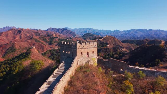 High angle view of the historic Great Wall of China winding across autumn hills with stone watchtowers under a clear blue sky