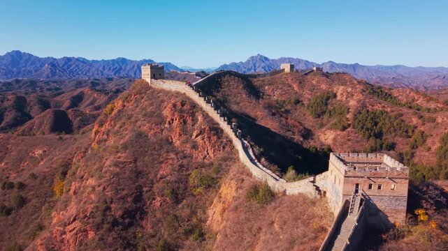 High angle view of the historic Great Wall of China winding across autumn hills with stone watchtowers under a clear blue sky