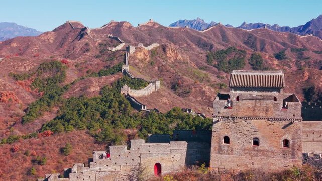 High angle view of the historic Great Wall of China winding across autumn hills with stone watchtowers under a clear blue sky