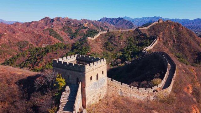 High angle view of the historic Great Wall of China winding across autumn hills with stone watchtowers under a clear blue sky